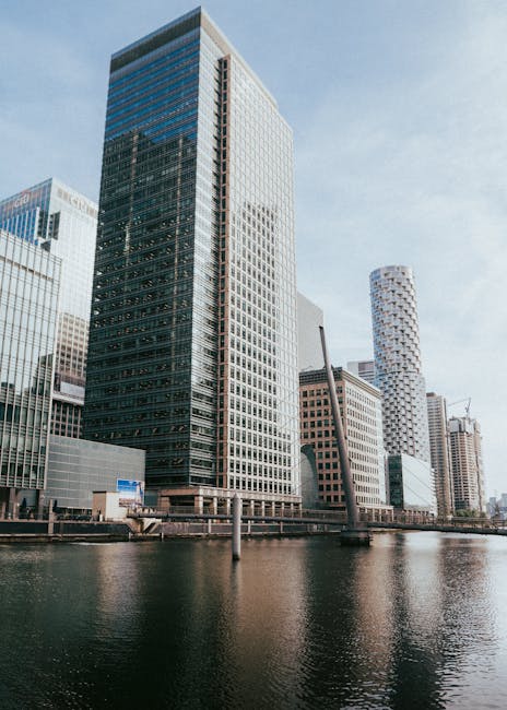 A panoramic view of a modern city skyline featuring numerous high-rise office buildings and skyscrapers, including structures with glass facades reflecting sunlight, with some branded with visible log
